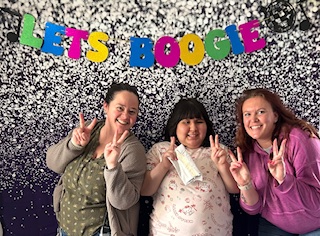  Two educators and a student are holding up peace signs while taking a picture in front of a photo w